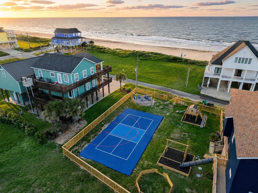 Blue pickleball and basketball court beside a beach house at sunset