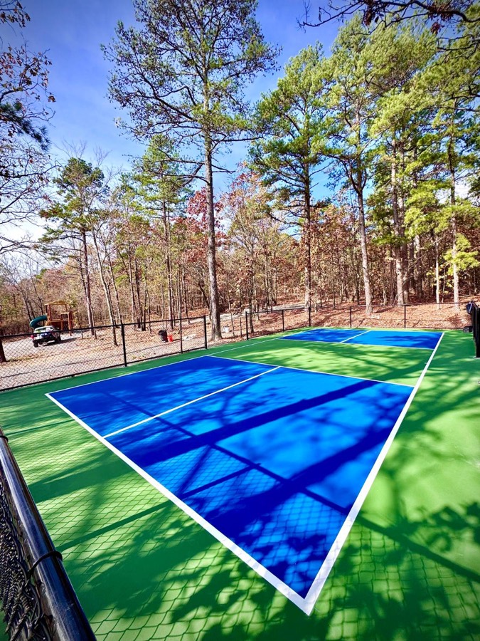 Blue and green pickleball court with fencing and pine trees