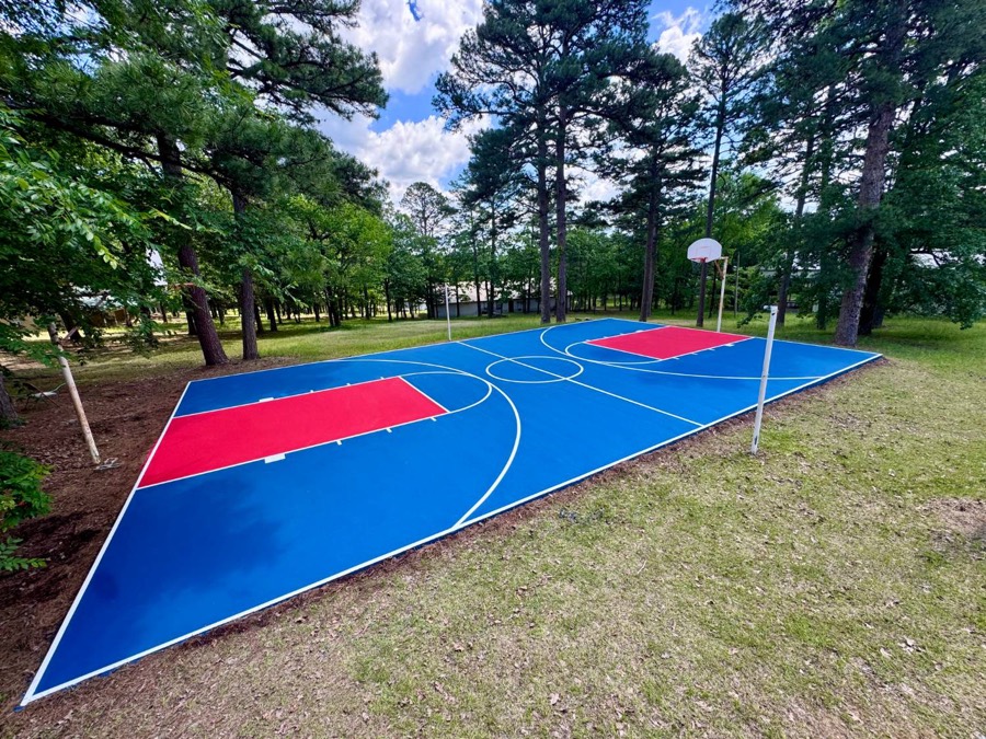 Blue and red full basketball court surrounded by pine trees